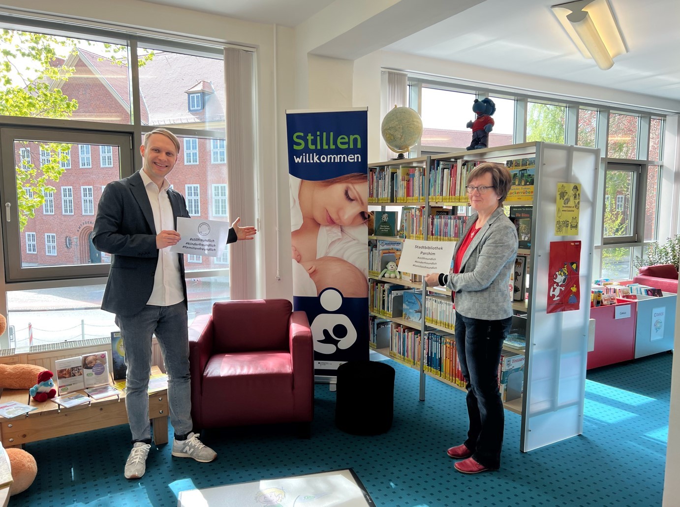 Uta Steglich, FD Jugend und Netzwerkkoordinatorin „Frühe Hilfe“ vom Landkreis Ludwigslust-Parchim und der neue Leiter der Parchimer Stadtbibliothek, Goran Misaljevic, präsentieren den „Stillfreundlichen Ort Stadtbibliothek Parchim“