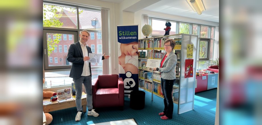 Uta Steglich, FD Jugend und Netzwerkkoordinatorin „Frühe Hilfe“ vom Landkreis Ludwigslust-Parchim und der neue Leiter der Parchimer Stadtbibliothek, Goran Misaljevic, präsentieren den „Stillfreundlichen Ort Stadtbibliothek Parchim“