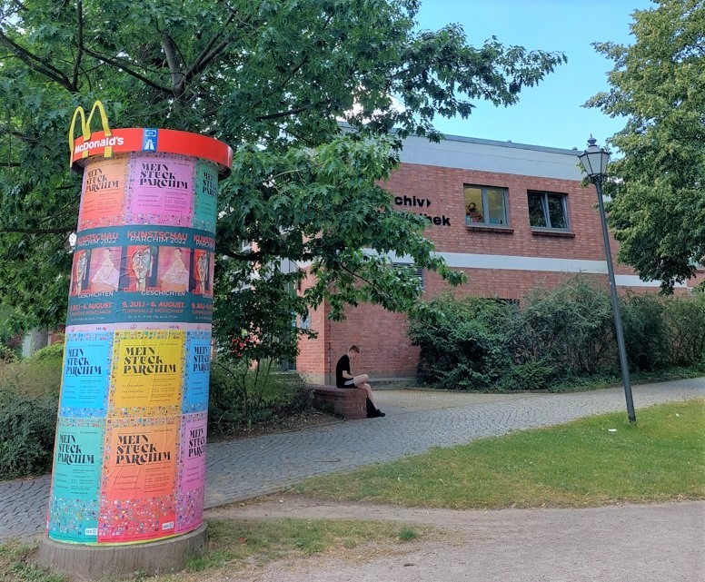 Werbesäule mit der Ausstellung "Mein Stück Parchim", im Hintergrund die Stadtbibliothek 